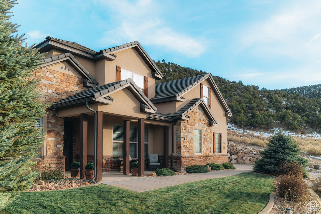 View of property exterior featuring stone siding, stucco siding, a yard, and a tile roof