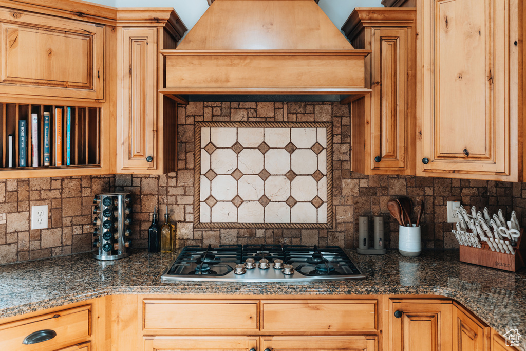 Kitchen with stainless steel gas stovetop, tasteful backsplash, premium range hood, and dark countertops