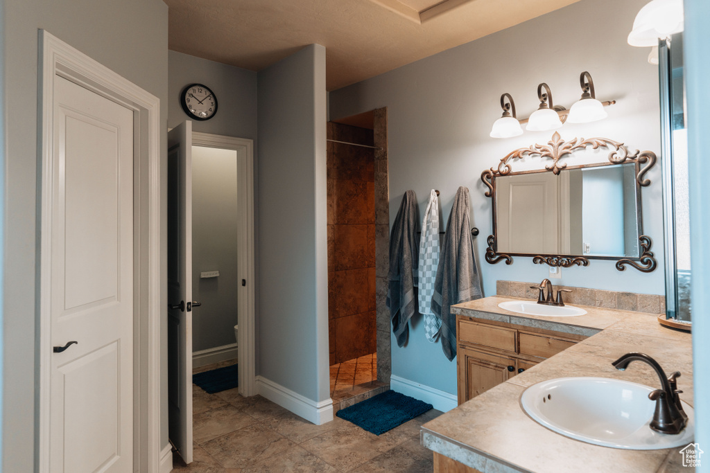 Full bathroom with a tile shower, double vanity, and baseboards