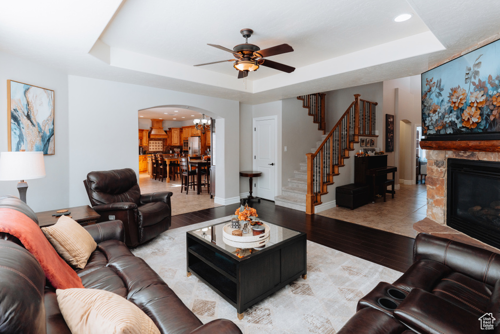 Living room featuring arched walkways, a raised ceiling, a ceiling fan, light wood-style floors, and stairway