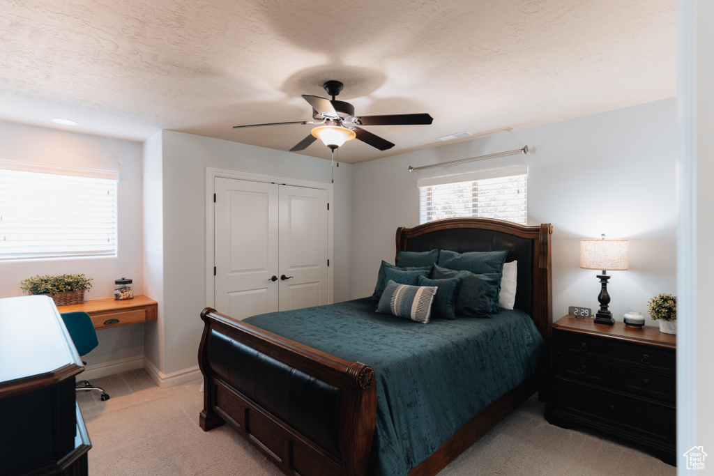 Bedroom with light colored carpet, an office area, baseboards, a closet, and a ceiling fan