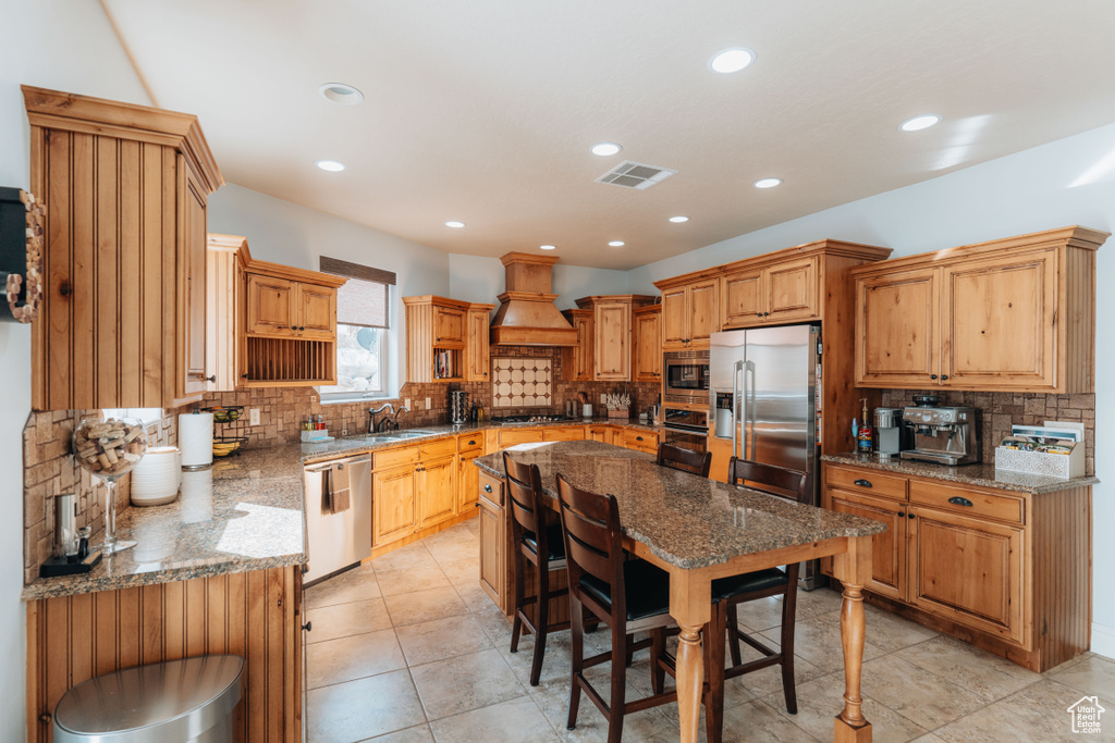 Kitchen featuring stainless steel appliances, a sink, custom range hood, decorative backsplash, and stone counters