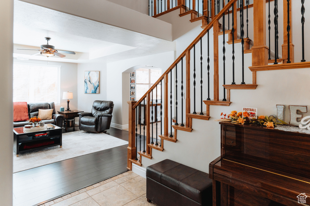 Stairway with arched walkways, a ceiling fan, baseboards, and a tray ceiling