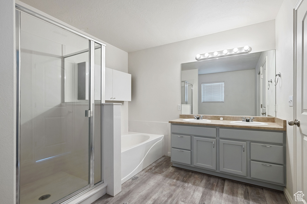 Bathroom with a stall shower, wood finished floors, a garden tub, and double vanity