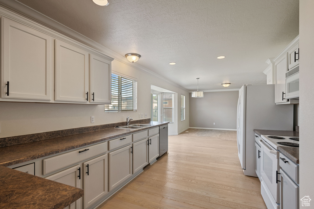 Kitchen with white appliances, a sink, dark countertops, light wood-style floors, and crown molding