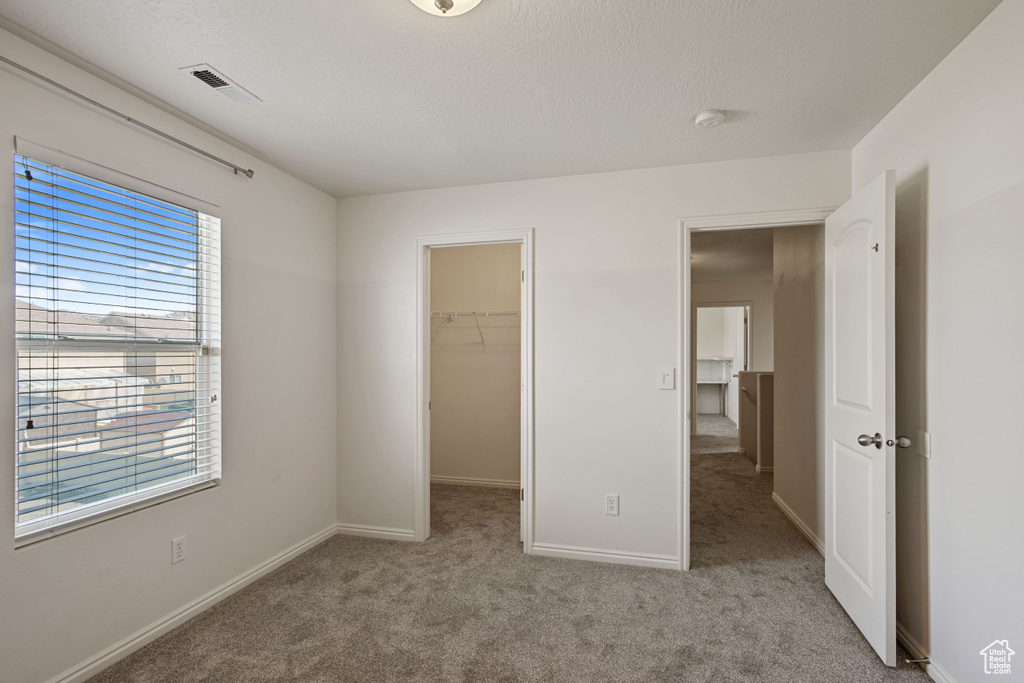 Unfurnished bedroom with carpet flooring, a walk in closet, baseboards, and a closet