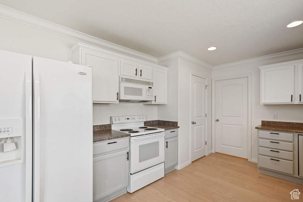 Kitchen featuring white appliances, dark countertops, light wood-style floors, crown molding, and recessed lighting