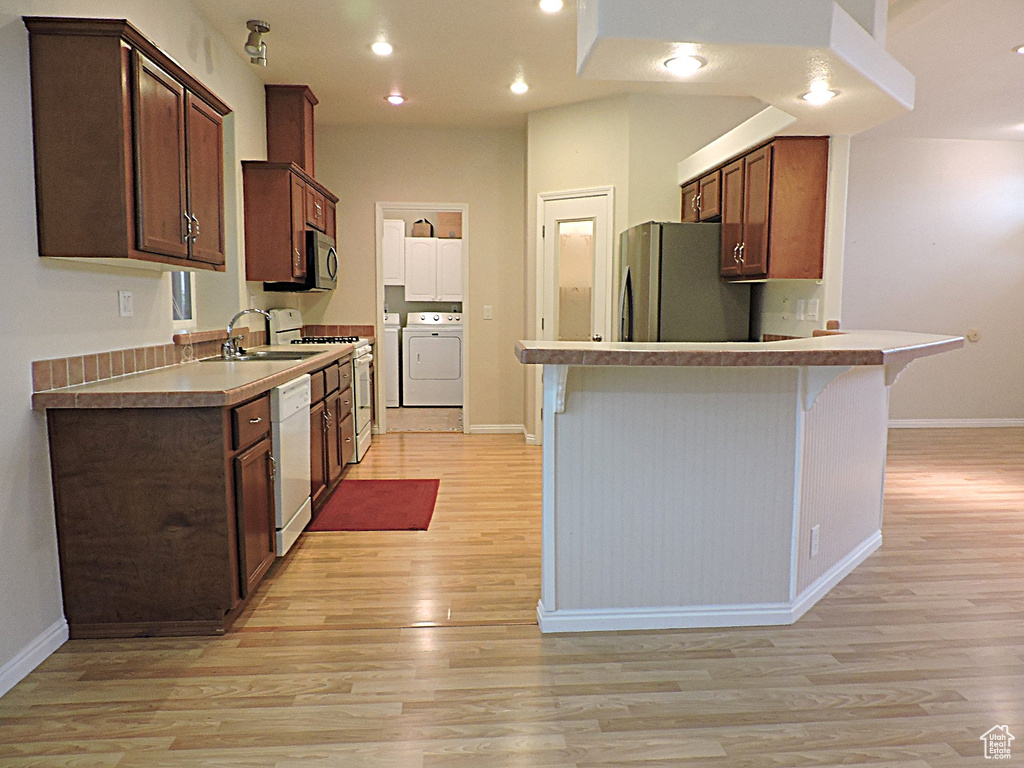 Kitchen featuring white appliances, washing machine and dryer, a sink, light wood-type flooring, and baseboards