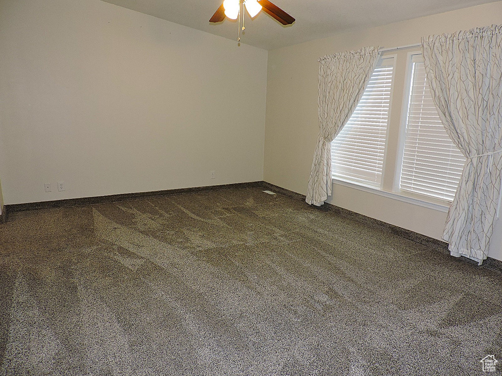 Unfurnished room featuring a ceiling fan, dark carpet, and baseboards