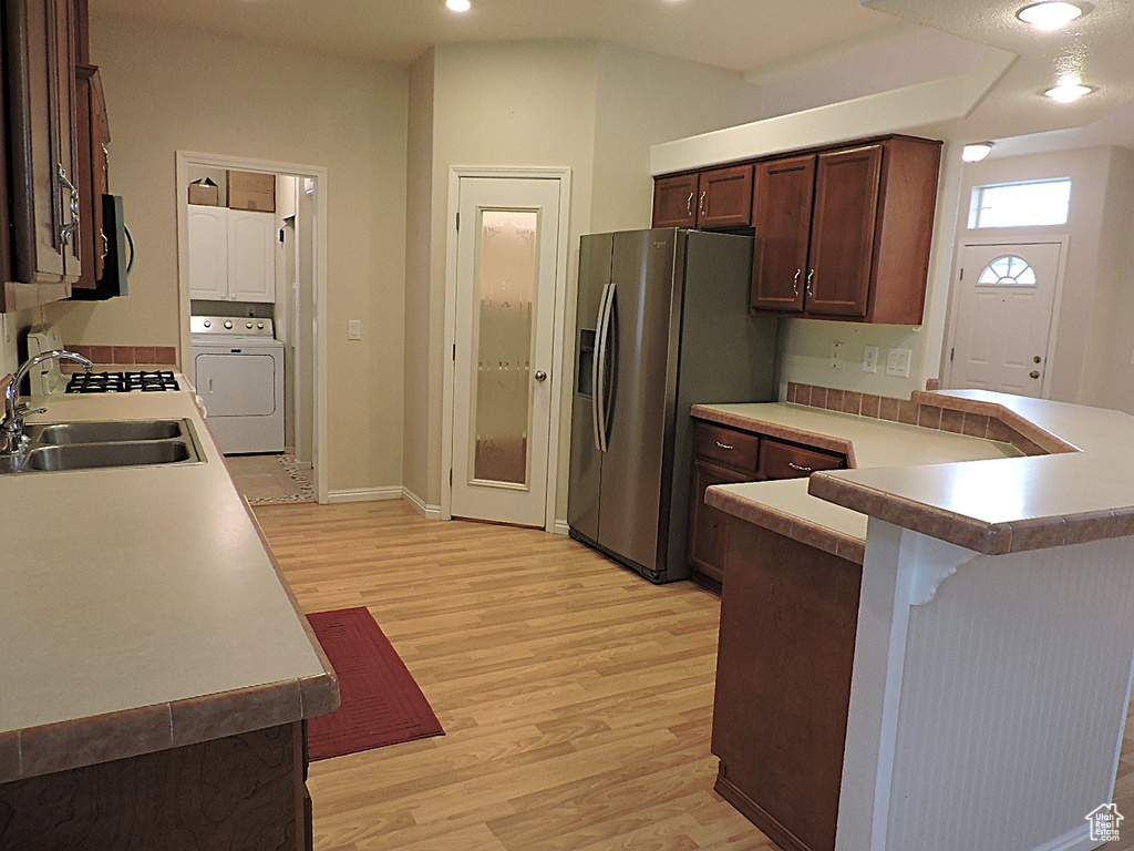 Kitchen featuring a sink, washer / dryer, light wood-type flooring, stainless steel refrigerator with ice dispenser, and a breakfast bar area