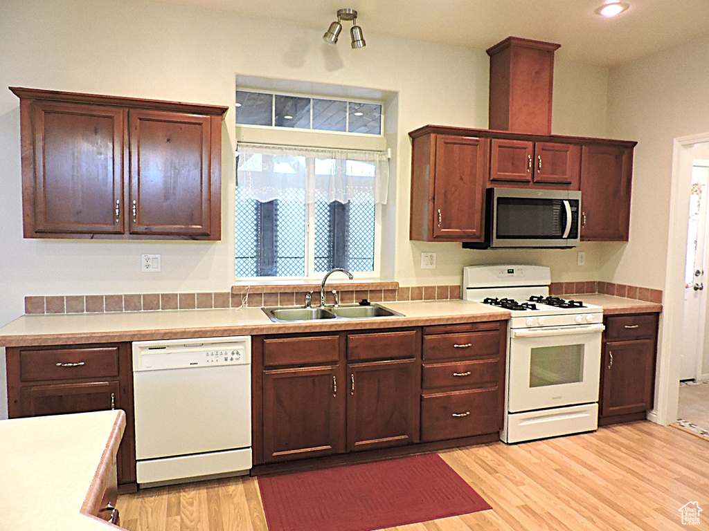Kitchen featuring white appliances, a sink, light wood finished floors, recessed lighting, and light countertops