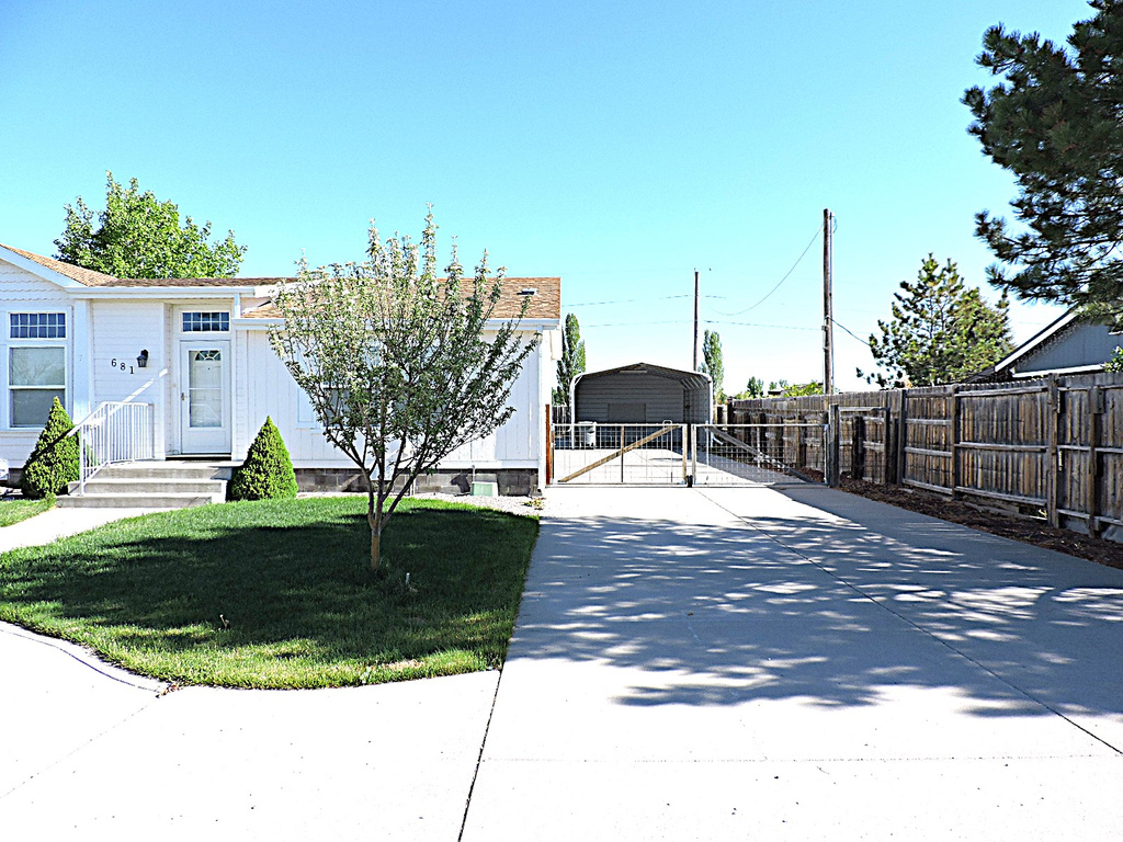 View of front of house featuring concrete driveway, a detached carport, and a gate