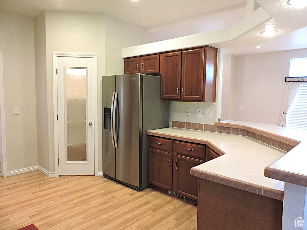 Kitchen with stainless steel refrigerator with ice dispenser, light wood-style flooring, a peninsula, light countertops, and dark brown cabinetry
