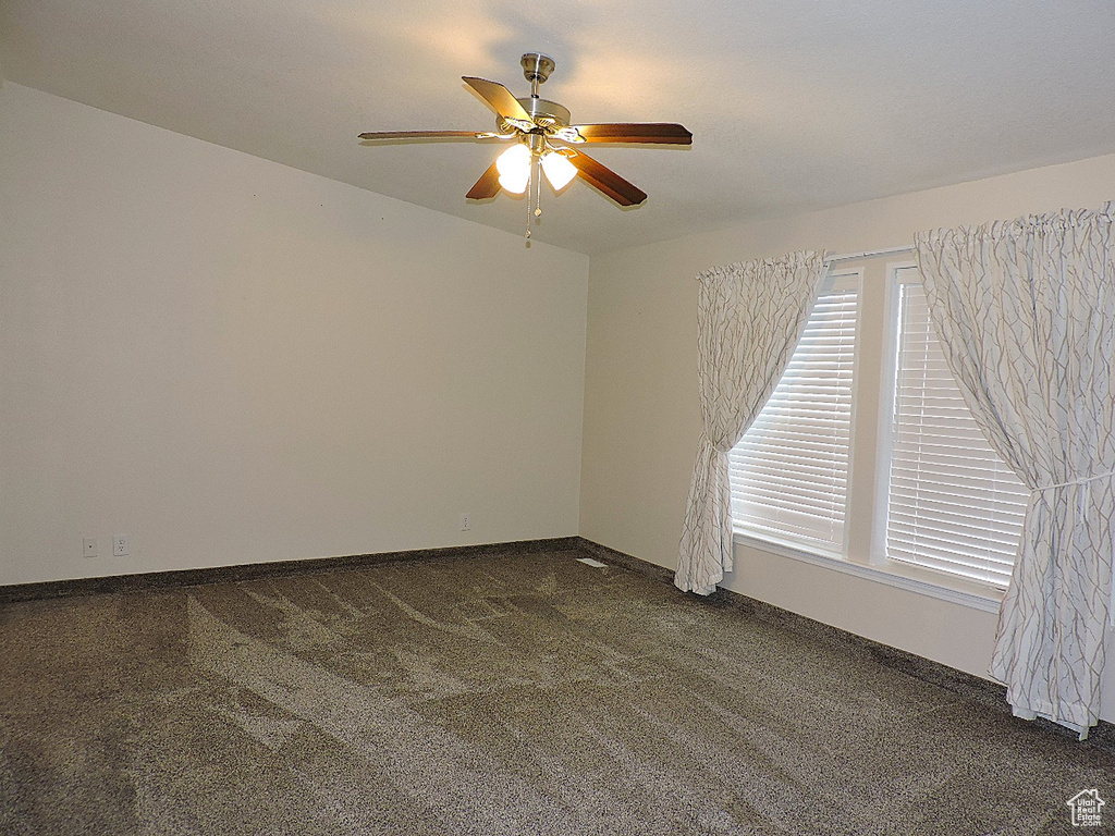 Spare room with dark colored carpet, ceiling fan, and baseboards