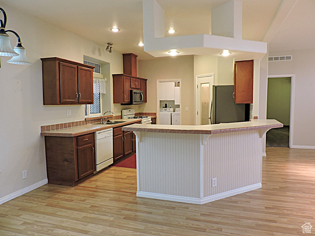 Kitchen with appliances with stainless steel finishes, light wood finished floors, a kitchen bar, a peninsula, and a sink