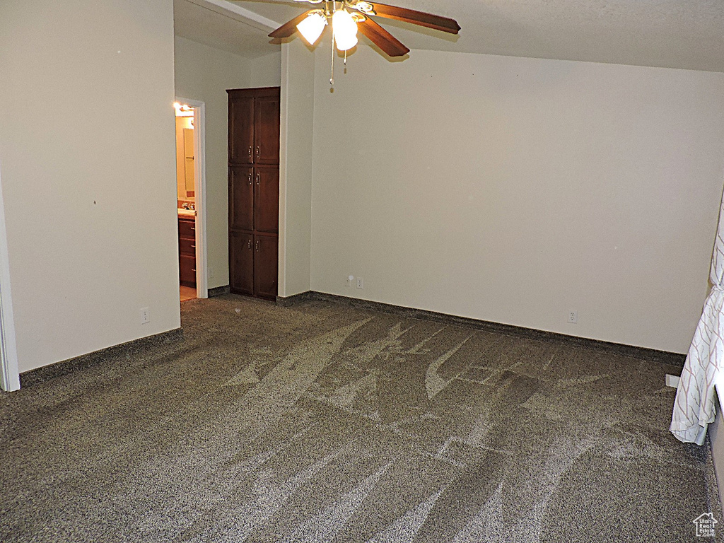 Empty room with dark carpet, a ceiling fan, and baseboards