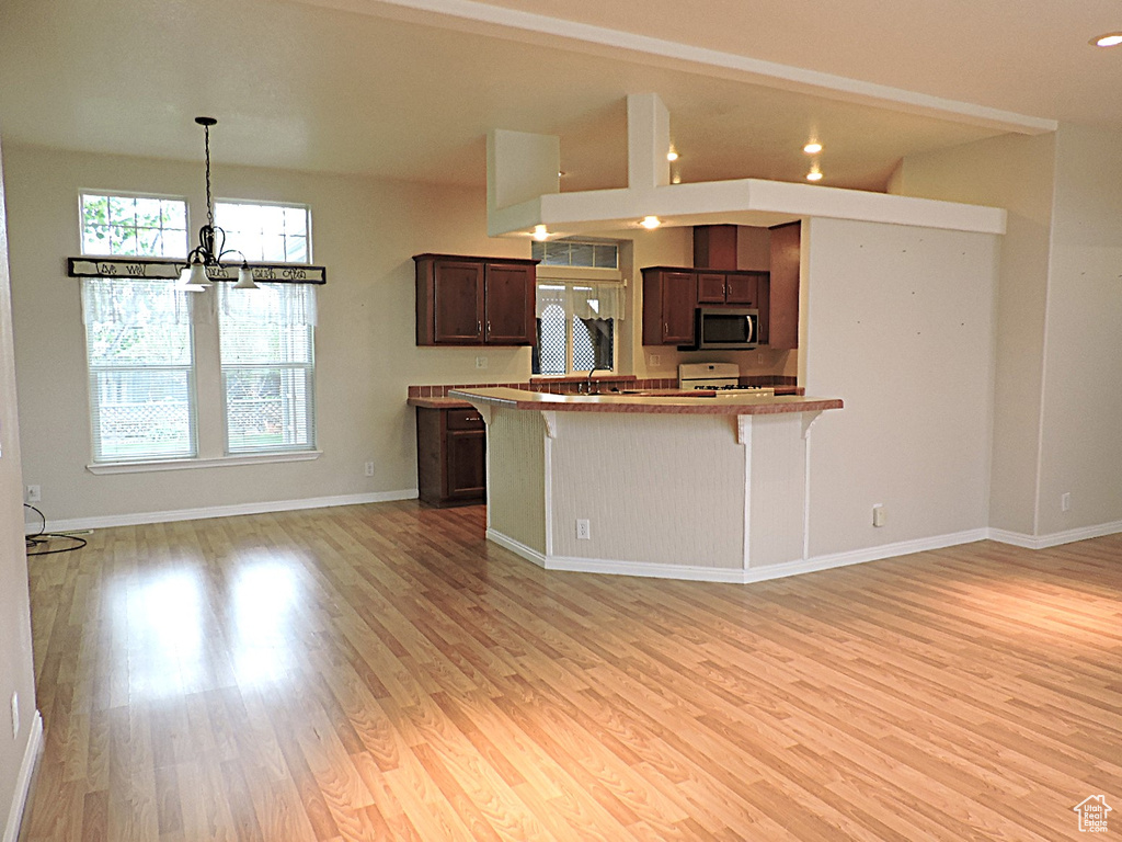 Kitchen featuring stainless steel microwave, a breakfast bar area, a chandelier, light wood-style flooring, and recessed lighting