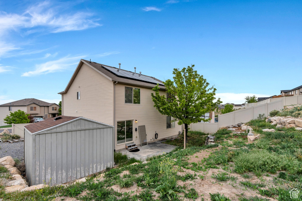 Back of house with a patio area, an outdoor structure, a storage unit, a fenced backyard, and solar panels