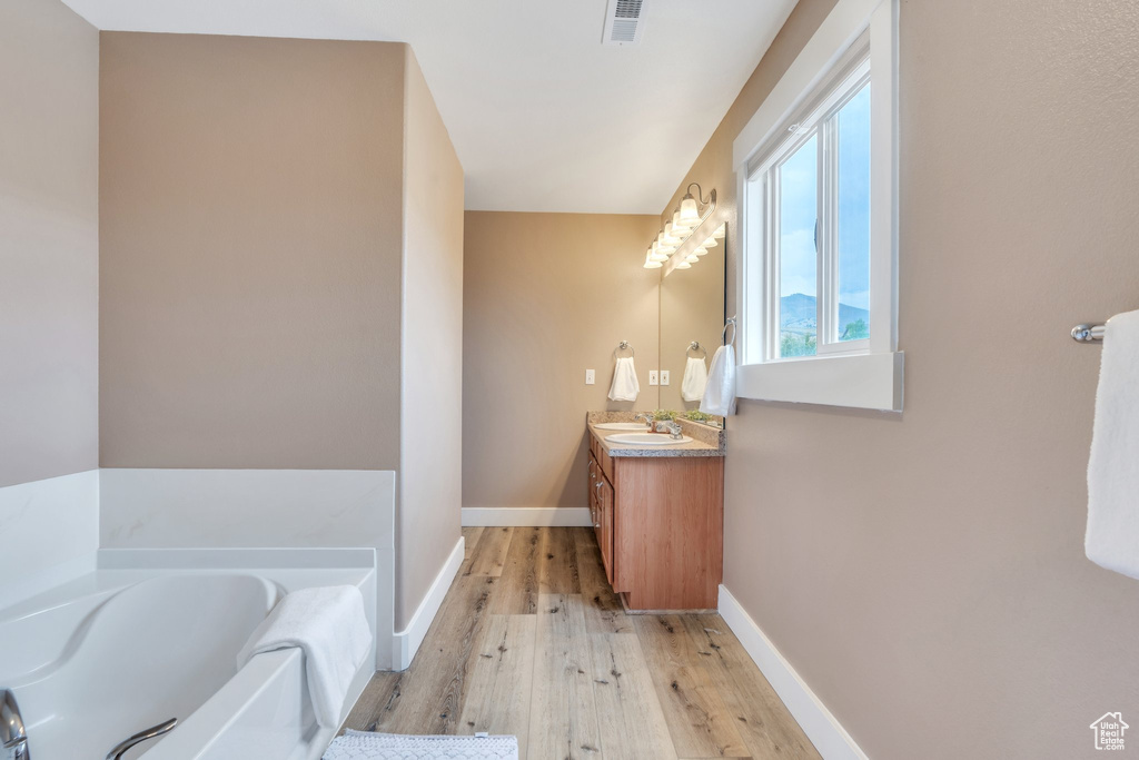 Bathroom featuring baseboards, visible vents, a bath, vanity, and wood finished floors