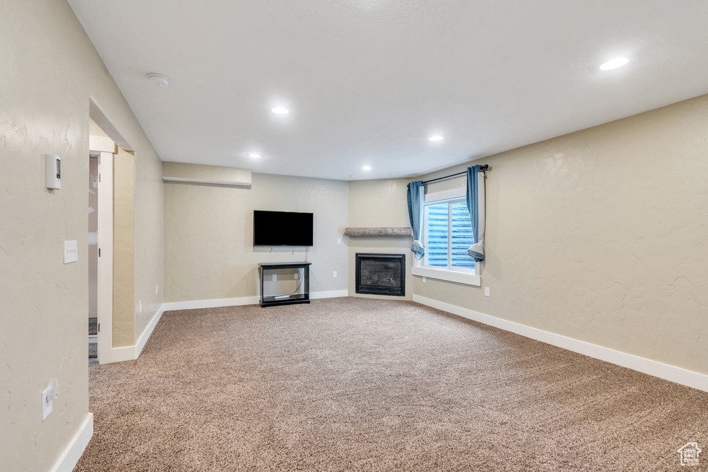 Unfurnished living room with carpet flooring, recessed lighting, baseboards, and a glass covered fireplace