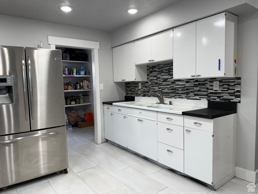 Kitchen with stainless steel fridge, tasteful backsplash, white cabinetry, recessed lighting, and a sink