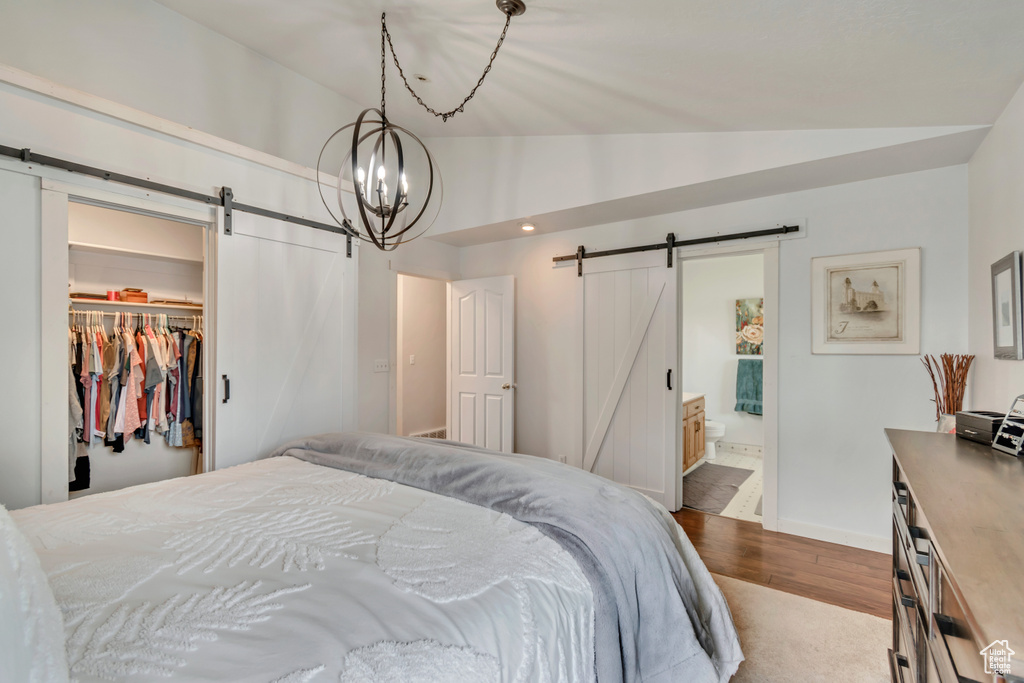 Bedroom with a barn door, lofted ceiling, dark wood-type flooring, a walk in closet, and baseboards