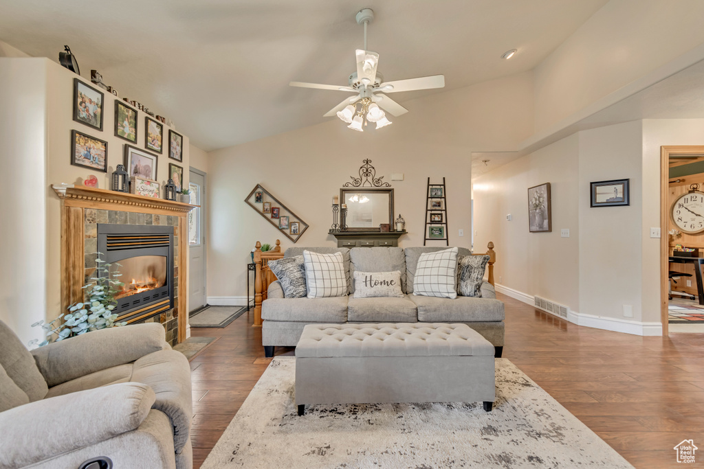 Living room with wood finished floors, a tiled fireplace, baseboards, a ceiling fan, and vaulted ceiling