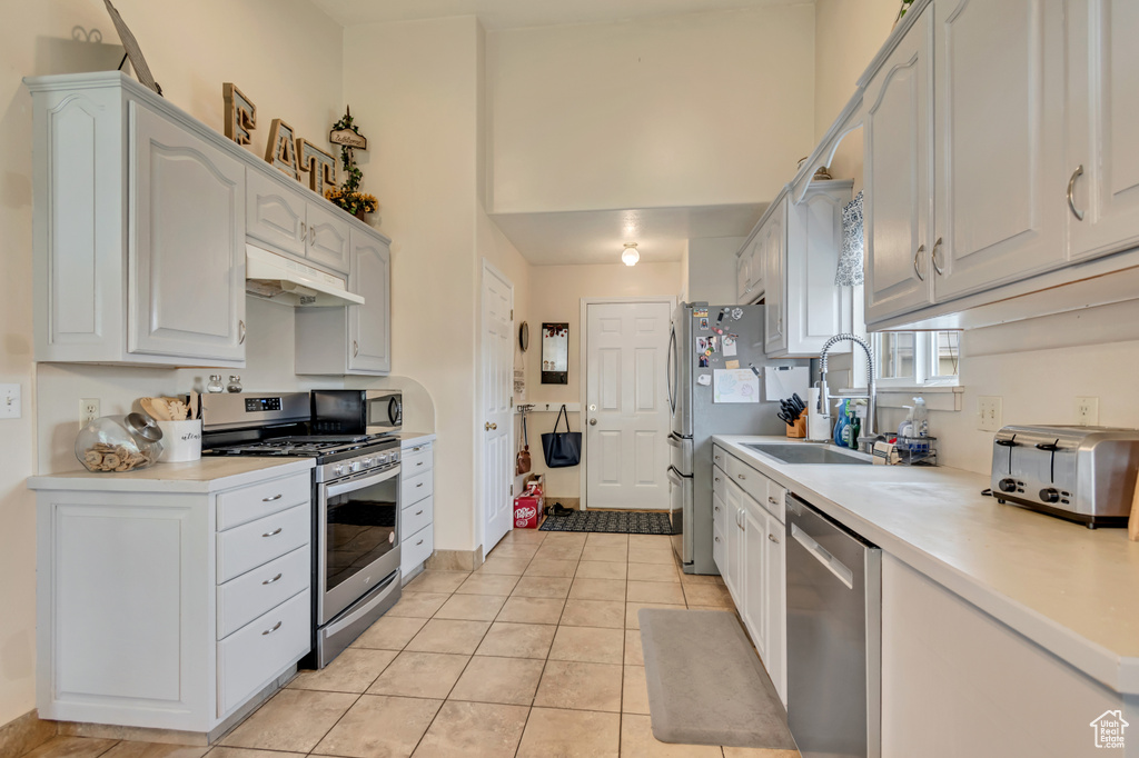 Kitchen featuring appliances with stainless steel finishes, under cabinet range hood, light tile patterned flooring, light countertops, and a sink