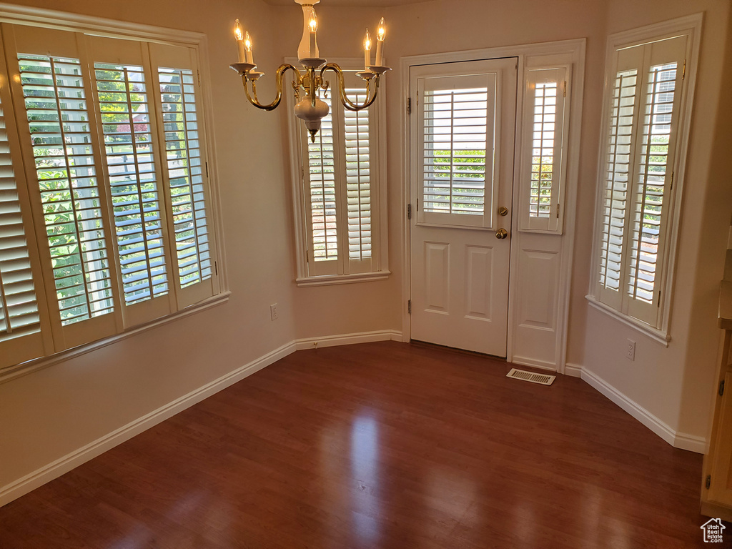 Unfurnished dining area featuring a chandelier, dark wood-style floors, baseboards, and plenty of natural light