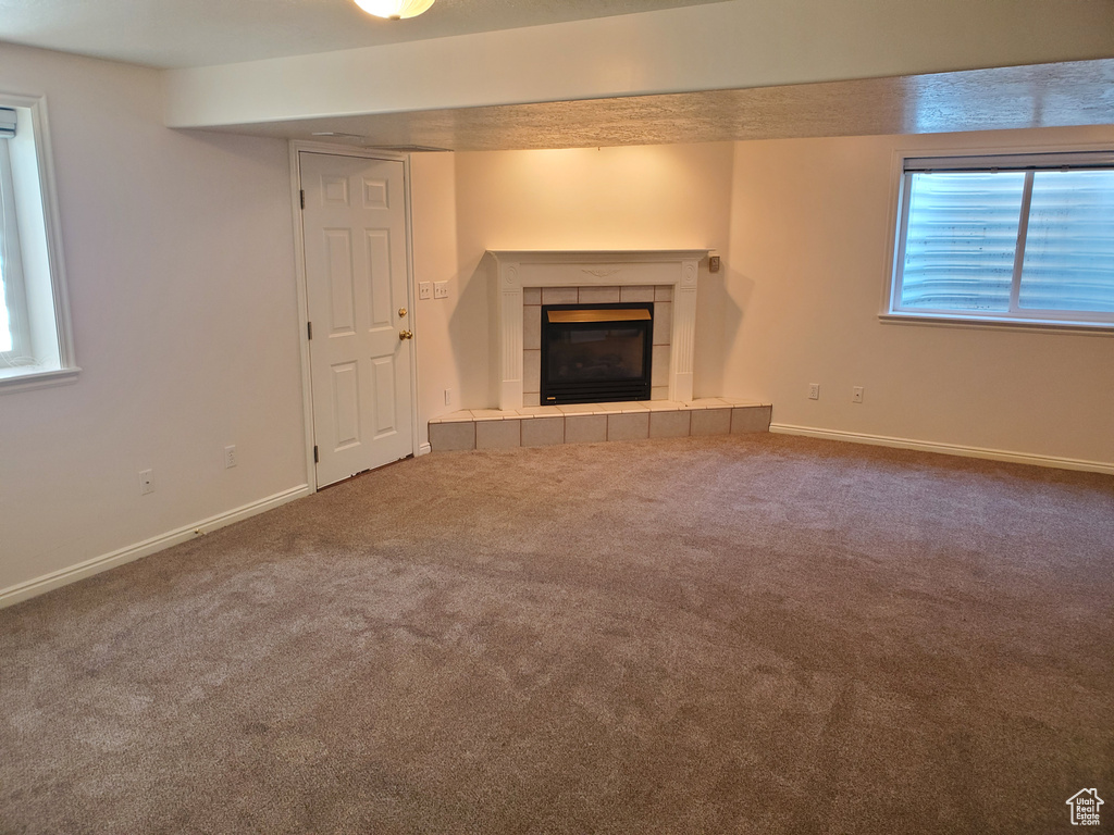 Unfurnished living room featuring a tiled fireplace, carpet, and baseboards