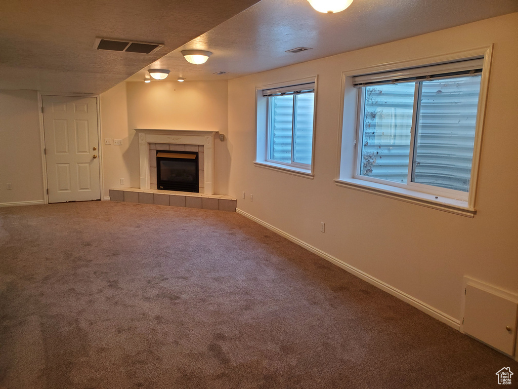 Unfurnished living room with carpet floors, a fireplace, baseboards, and a textured ceiling