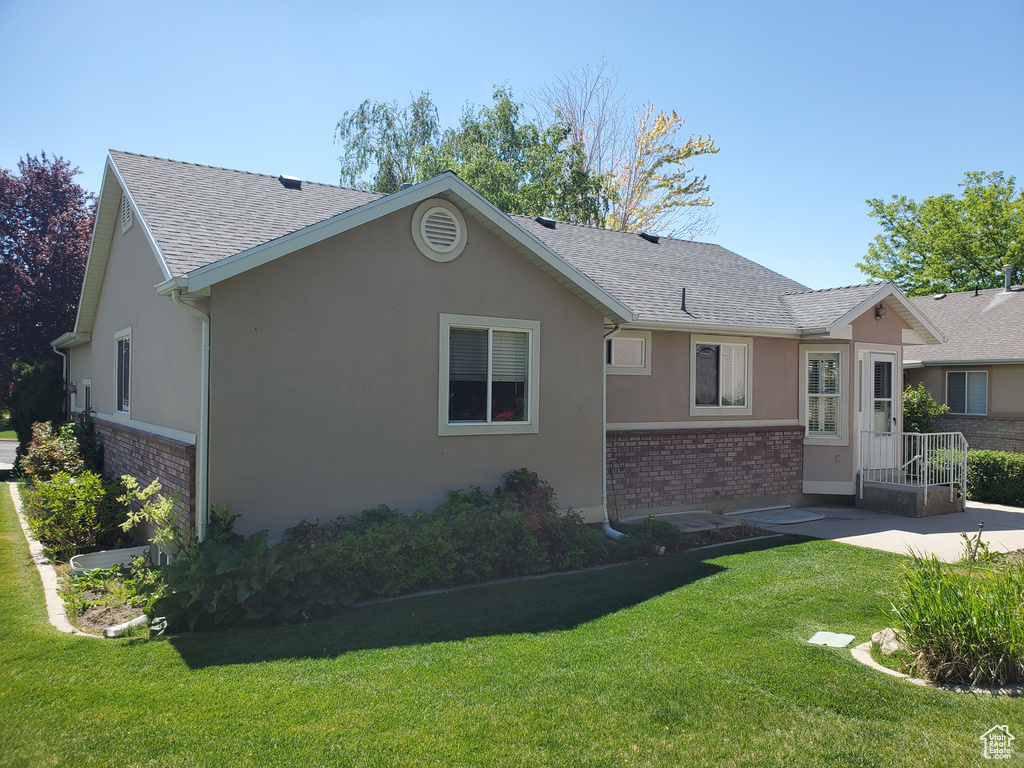 View of front of house with brick siding, a shingled roof, stucco siding, a front lawn, and a patio