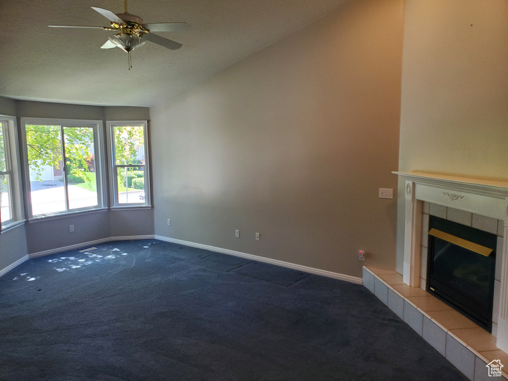 Unfurnished living room featuring carpet floors, baseboards, vaulted ceiling, ceiling fan, and a tile fireplace
