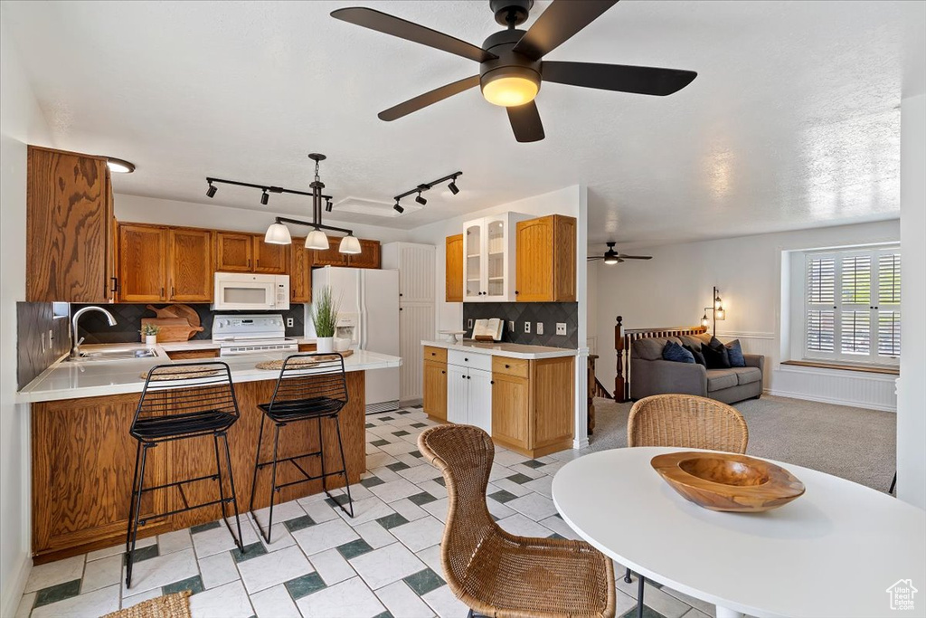 Kitchen featuring white appliances, a sink, a peninsula, ceiling fan, and light countertops