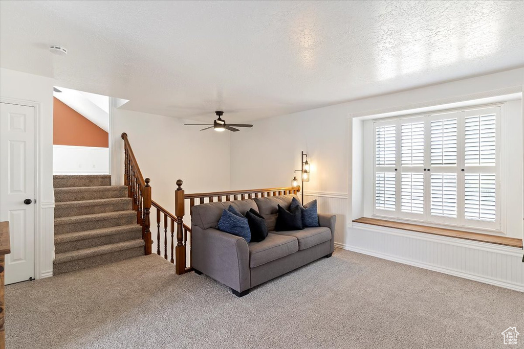 Carpeted living room with ceiling fan and stairs