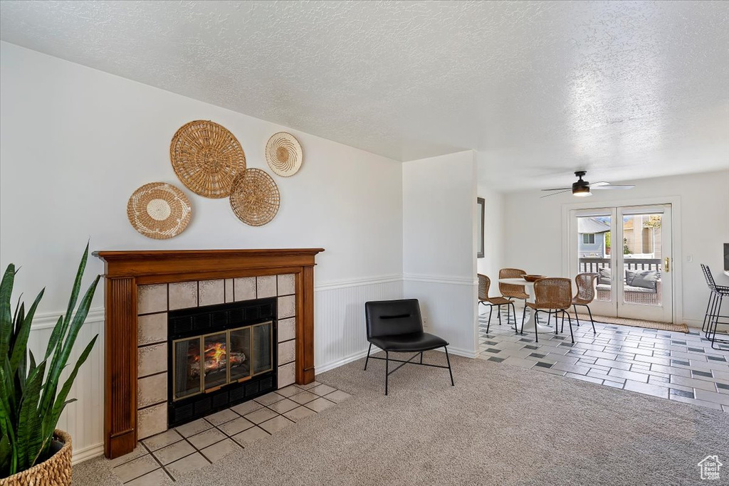 Living area with a ceiling fan, a textured ceiling, a tiled fireplace, and tile patterned floors
