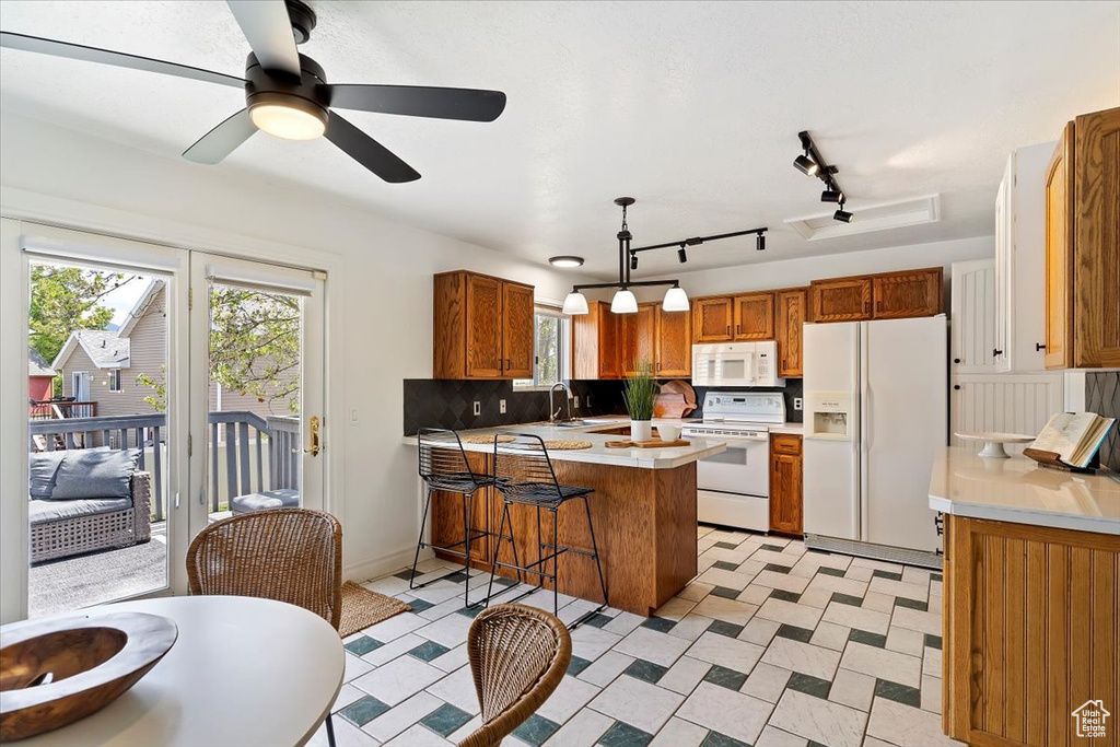 Kitchen with white appliances, a peninsula, a sink, light countertops, and ceiling fan