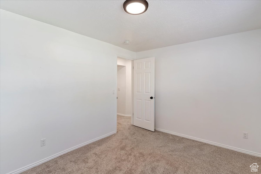 Empty room with light colored carpet, baseboards, and a smoke detector