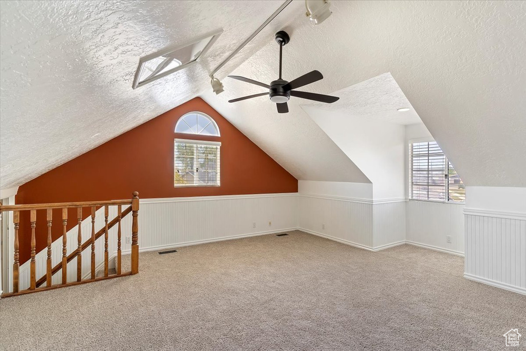 Additional living space with a textured ceiling, ceiling fan, plenty of natural light, carpet floors, and vaulted ceiling