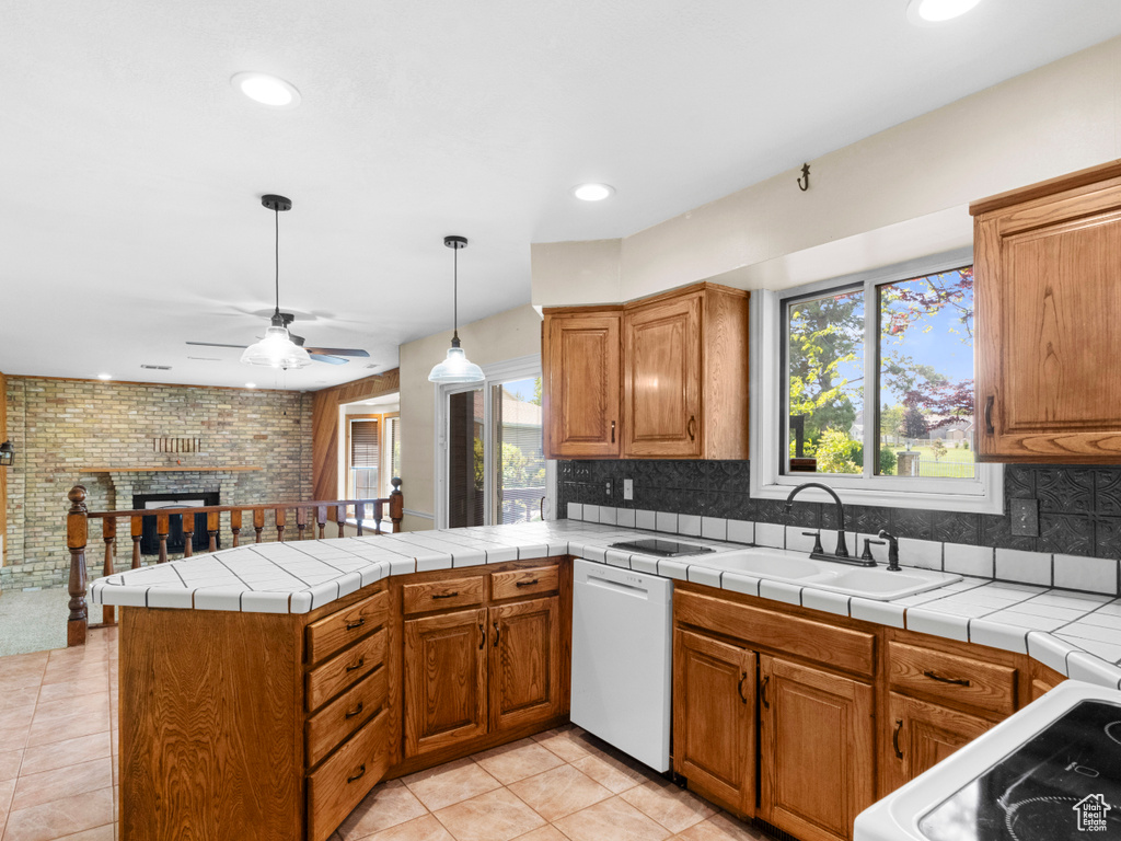 Kitchen with white dishwasher, a sink, a peninsula, a ceiling fan, and brown cabinetry