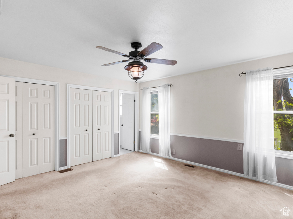 Unfurnished bedroom with two closets, carpet floors, baseboards, and a ceiling fan