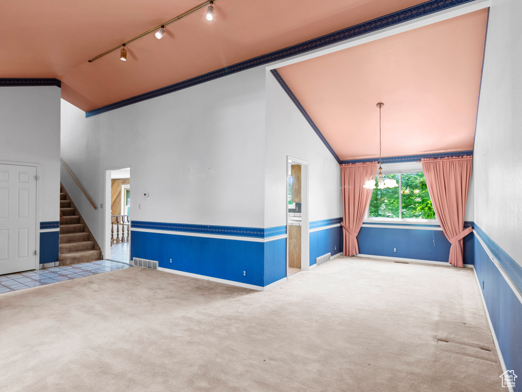 Carpeted spare room featuring vaulted ceiling, rail lighting, stairway, baseboards, and ornamental molding
