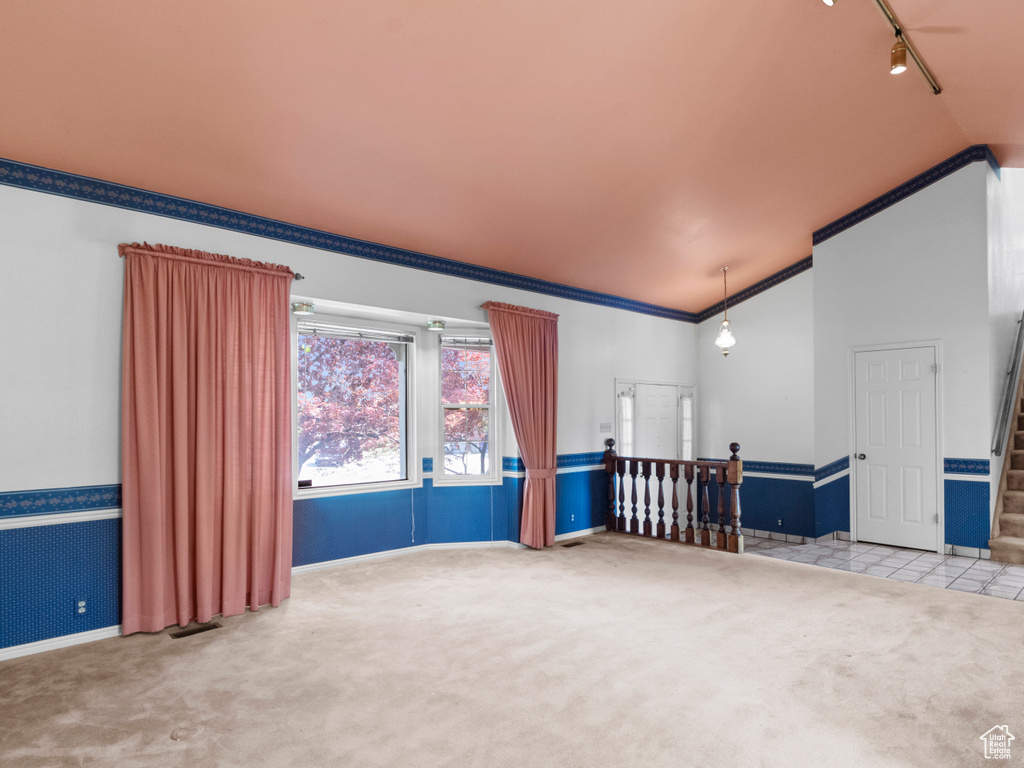 Carpeted empty room with lofted ceiling, crown molding, stairs, baseboards, and track lighting