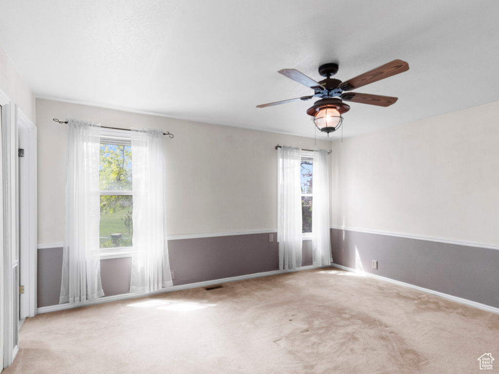 Carpeted empty room featuring ceiling fan, plenty of natural light, and baseboards