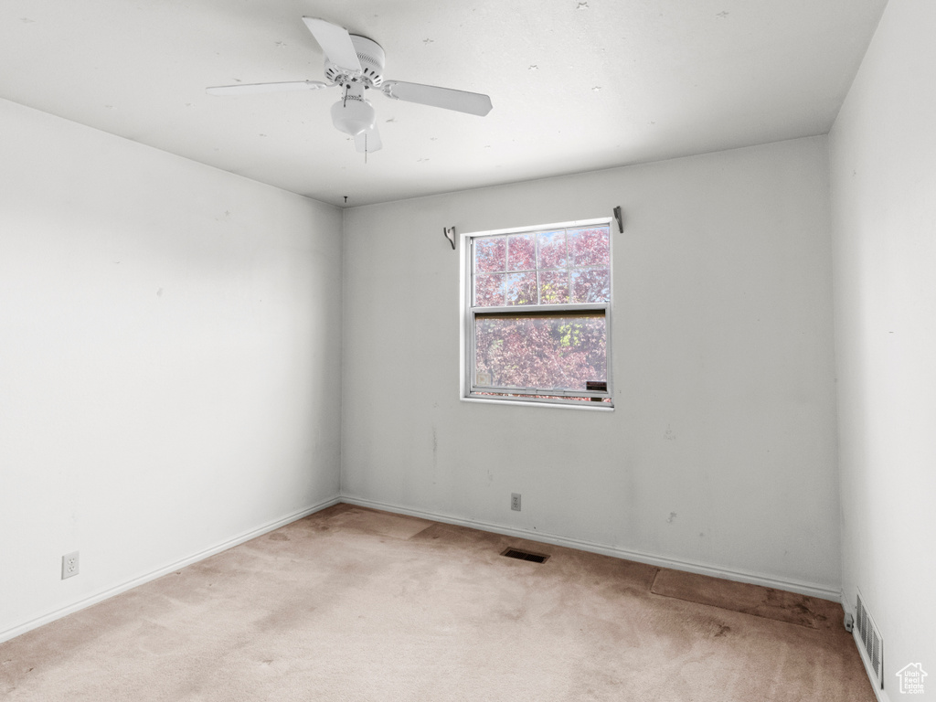 Spare room featuring light colored carpet, a ceiling fan, and baseboards