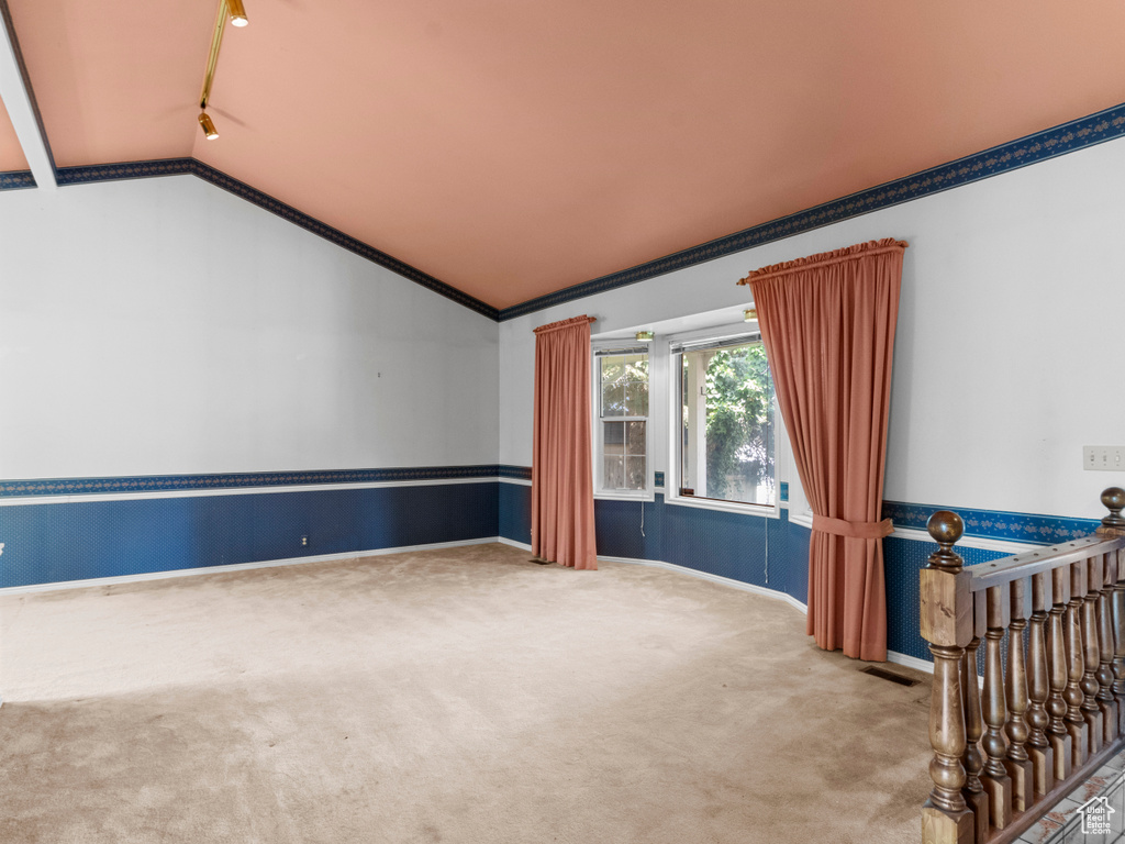 Spare room with carpet flooring, lofted ceiling, crown molding, baseboards, and track lighting