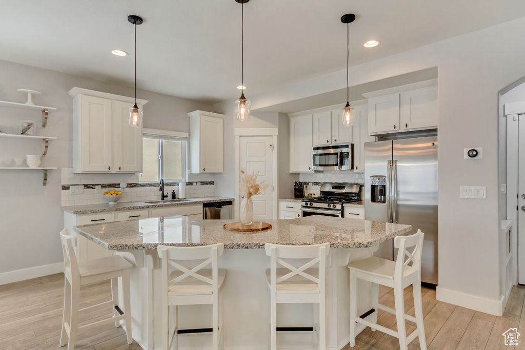 Kitchen featuring light wood-style floors, decorative backsplash, appliances with stainless steel finishes, and a sink