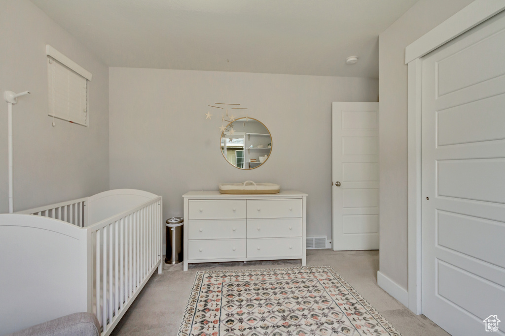 Bedroom with light colored carpet, visible vents, and a crib