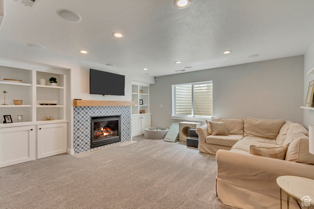 Carpeted living area featuring a tiled fireplace, built in features, and recessed lighting