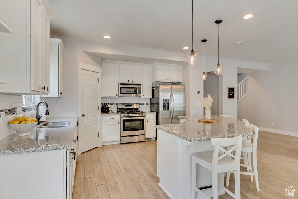 Kitchen with light wood-style flooring, a sink, white cabinetry, decorative backsplash, and stainless steel appliances
